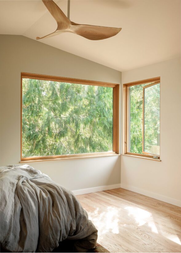 Bright ADU bedroom interior with corner windows and forest view